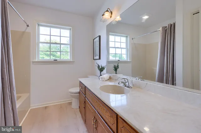 a bathroom with a granite countertop sink a toilet a large mirror and a window