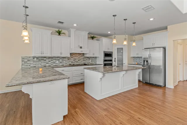 a kitchen with stainless steel appliances granite countertop a refrigerator a oven a sink and white cabinets with wooden floor