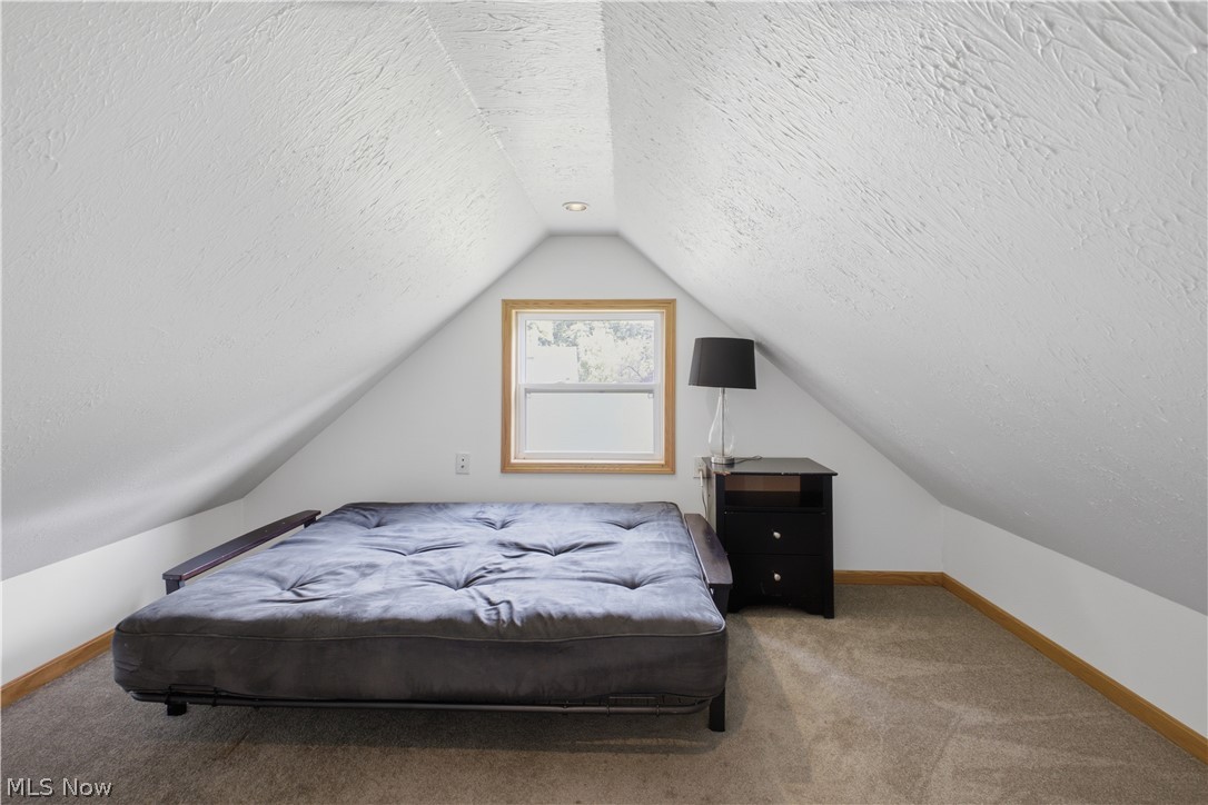1057 Center Road Clinton, OH 44216 - Photo 19 of 24 Attic bedroom featuring sloped ceilings, wood-trimmed casement window with natural light, wood-finish flooring, and built-in bedside table with integrated lamp fixture