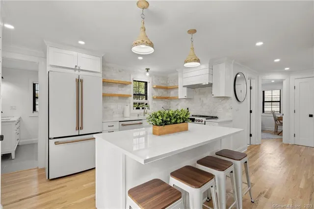 a kitchen with stainless steel appliances granite countertop a refrigerator a sink dishwasher a stove and a dining table with wooden floor