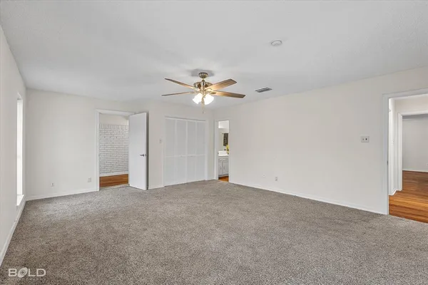 a view of an empty room with wooden floor and a ceiling fan