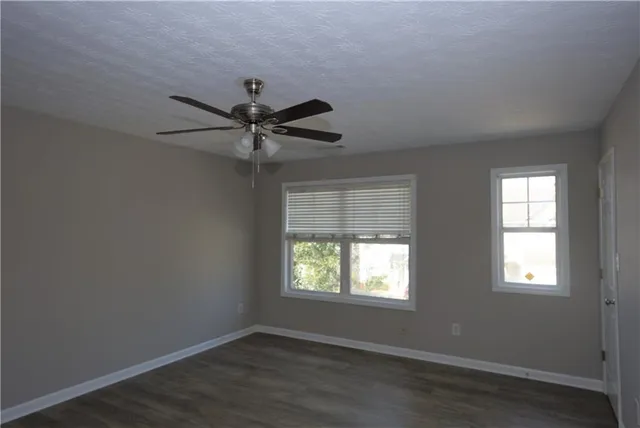 an empty room with wooden floor windows and fan