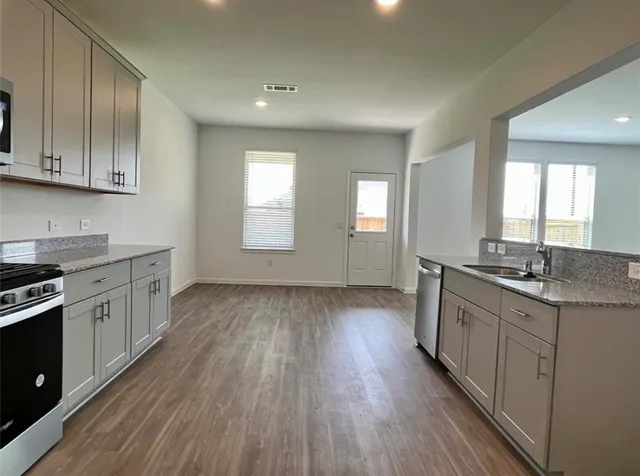 a kitchen with granite countertop a sink cabinets wooden floor and stainless steel appliances