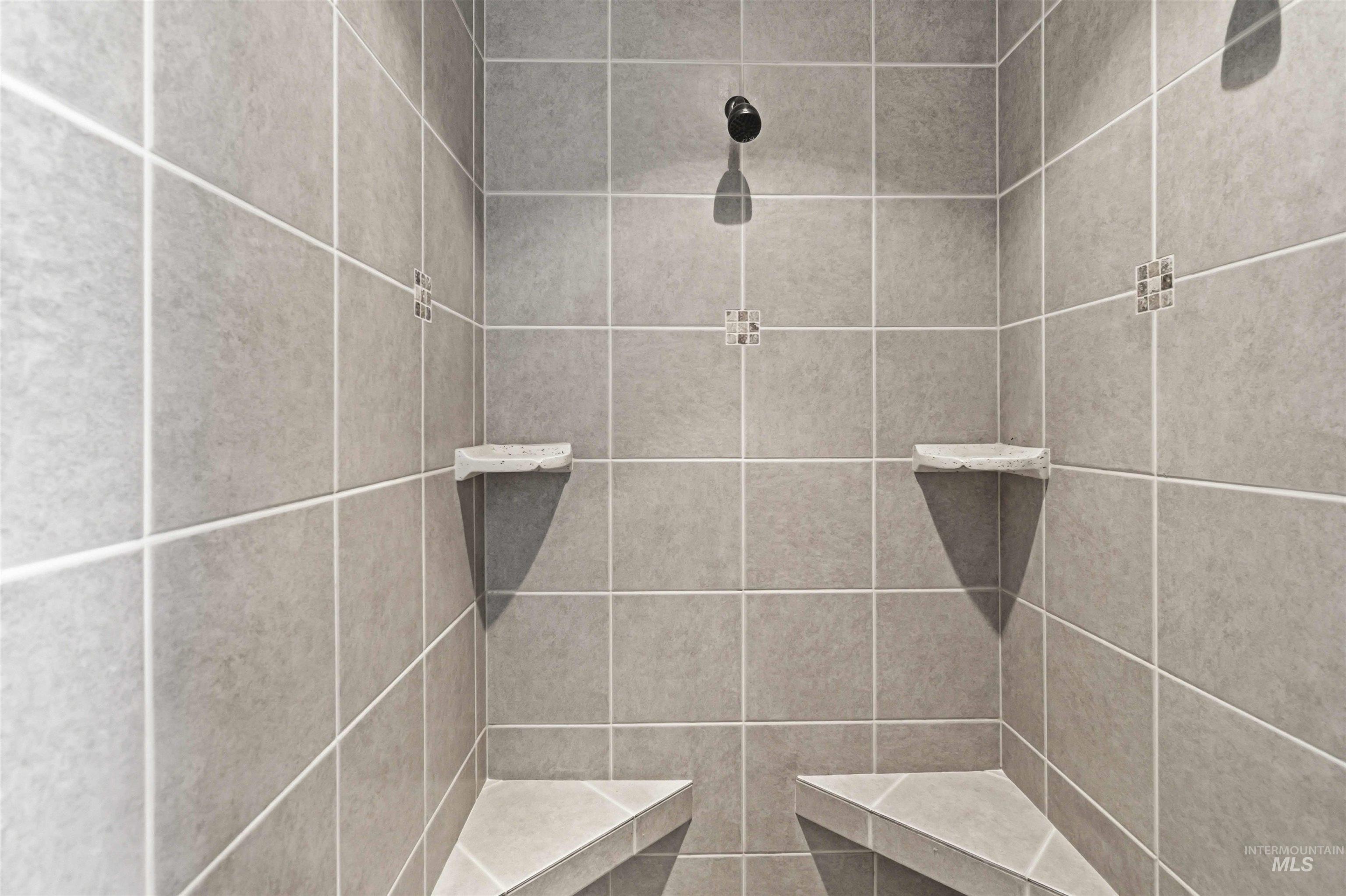 3218 North Cherry Laurel Way Star, ID 83669 - Photo 25 of 50 Shower enclosure featuring large format grey tile, integrated shower benches, corner shelving, decorative tile accents, and a fixed shower head