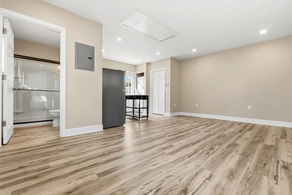 a view of an empty room with wooden floor and a kitchen