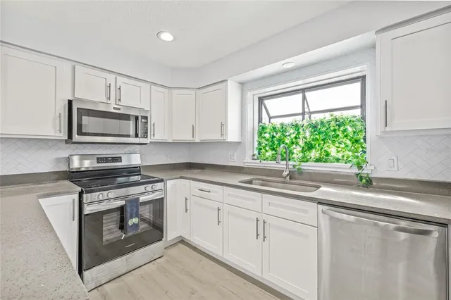 a kitchen with granite countertop white cabinets stainless steel appliances and a window
