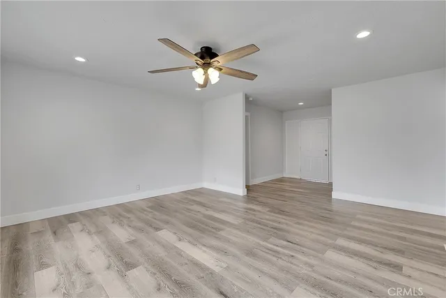 a view of an empty room with wooden floor and a ceiling fan