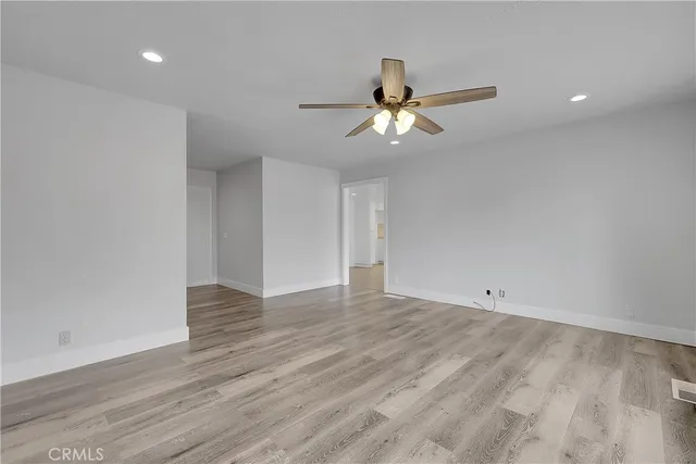 a view of an empty room with wooden floor and a ceiling fan