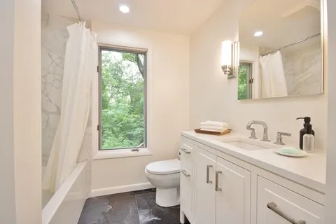 a bathroom with a toilet a sink a mirror a window and vanity