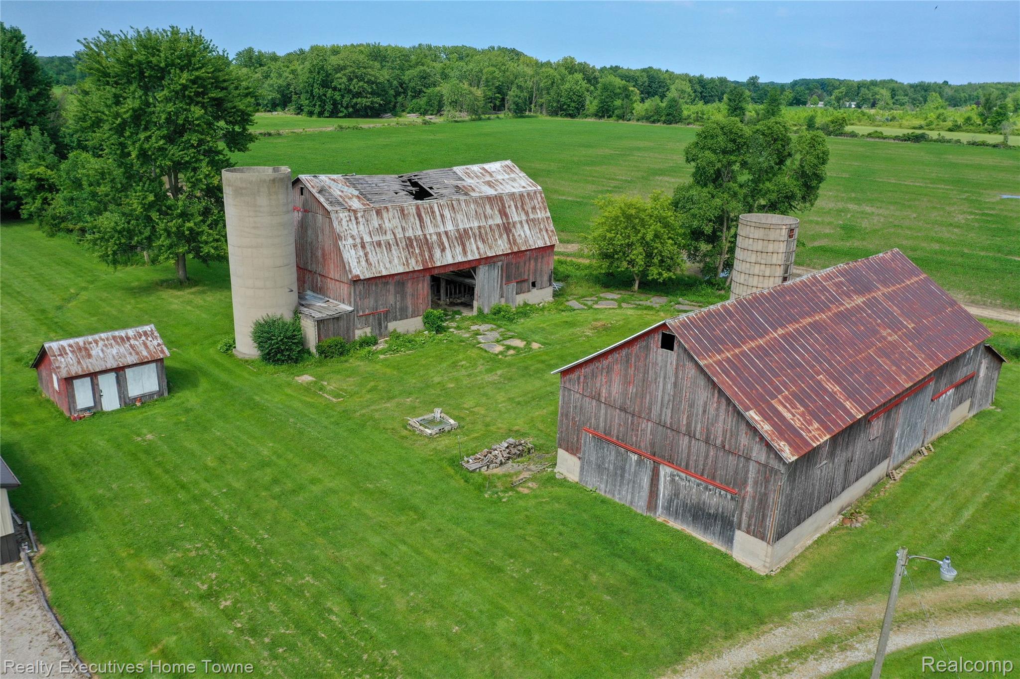 8728 Rynn Road Avoca, MI 48006 - Photo 35 of 53 Expansive green acreage featuring two large barns with corrugated metal roofing, an additional smaller outbuilding, and two silos