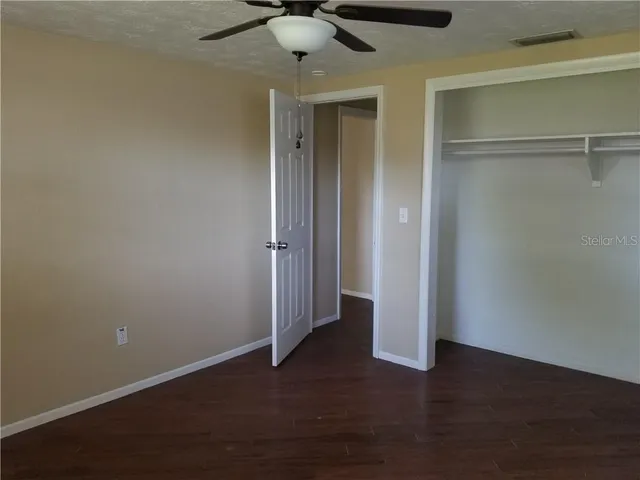 an empty room with wooden floor fan and windows