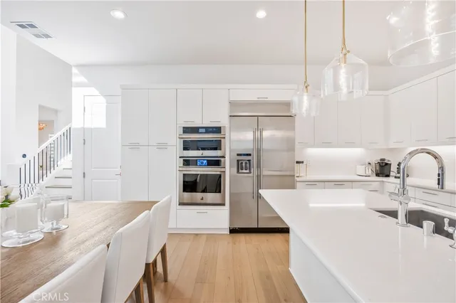 a large kitchen with kitchen island a stove a sink a refrigerator and white cabinets with wooden floor