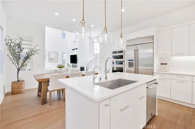 a kitchen with stainless steel appliances kitchen island granite countertop a sink a microwave a refrigerator and white cabinets with wooden floor