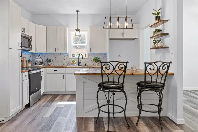 a kitchen with stainless steel appliances granite countertop a stove top oven a sink dishwasher and white cabinets with wooden floor