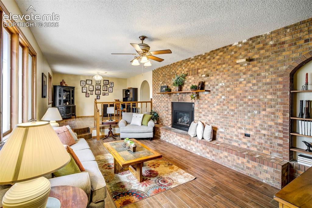 7585 Ponca Road Colorado Springs, CO 80908 - Photo 6 of 49 Living roomBeautiful wood plank tile flooring, brick walled gas fireplace, ceiling fan/light