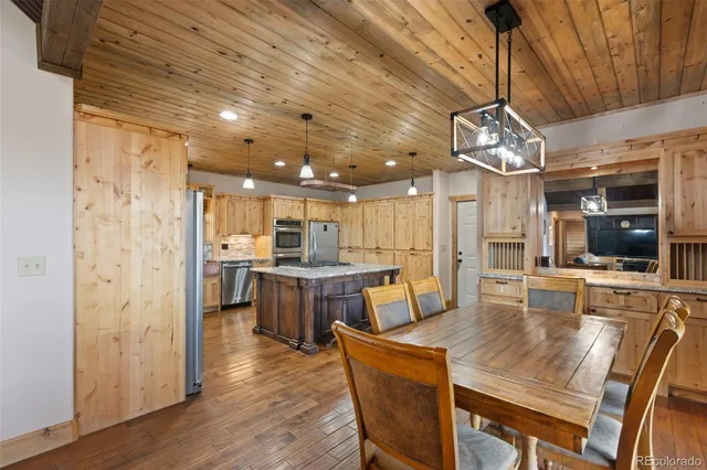 a dining room with stainless steel appliances kitchen island granite countertop a table chairs and a chandelier