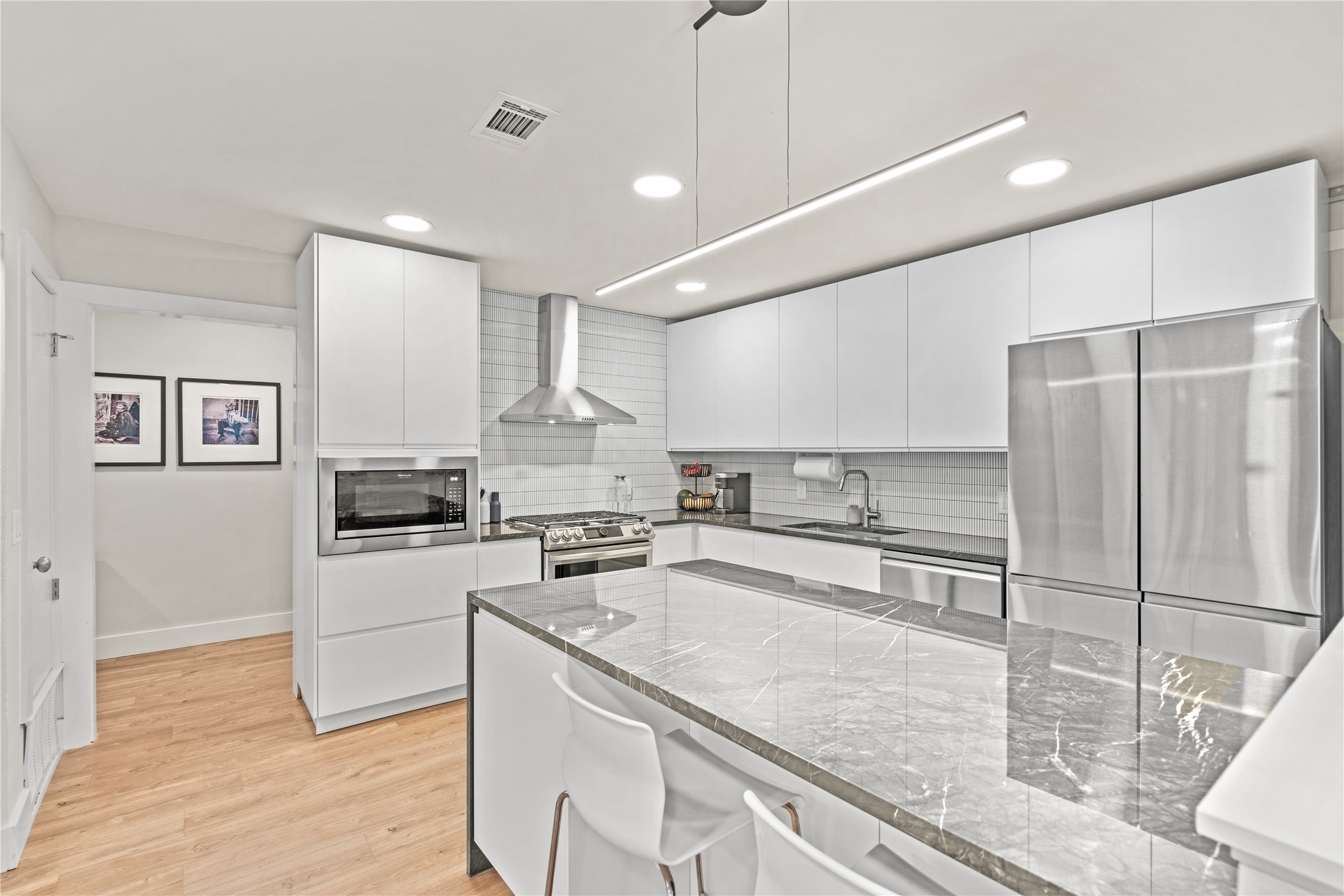 7107 Greenock Street Austin, TX 78749 - Photo 16 of 40 The kitchen features light wood flooring, white cabinetry, a stainless steel refrigerator, and a kitchen island with a stone countertop
