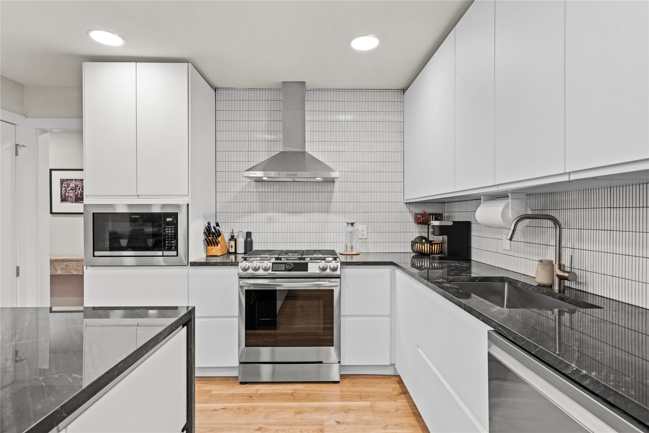 7107 Greenock Street Austin, TX 78749 - Photo 17 of 40 The kitchen features white cabinetry, stainless steel appliances, dark countertops, and light-toned backsplash tiling, all complemented by hardwood flooring