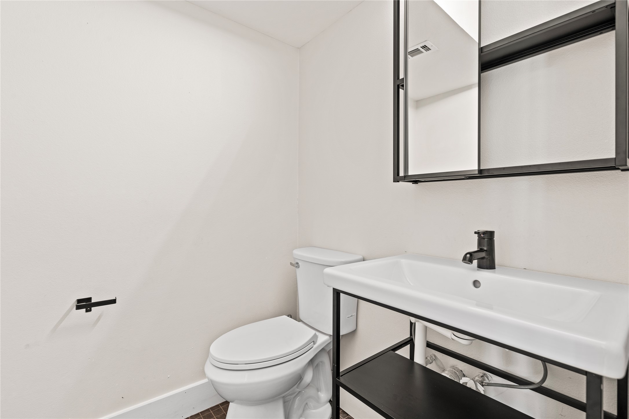 7107 Greenock Street Austin, TX 78749 - Photo 35 of 40 Bathroom featuring a white toilet, white wall-mounted sink with a black faucet, and a black framed mirrored cabinet