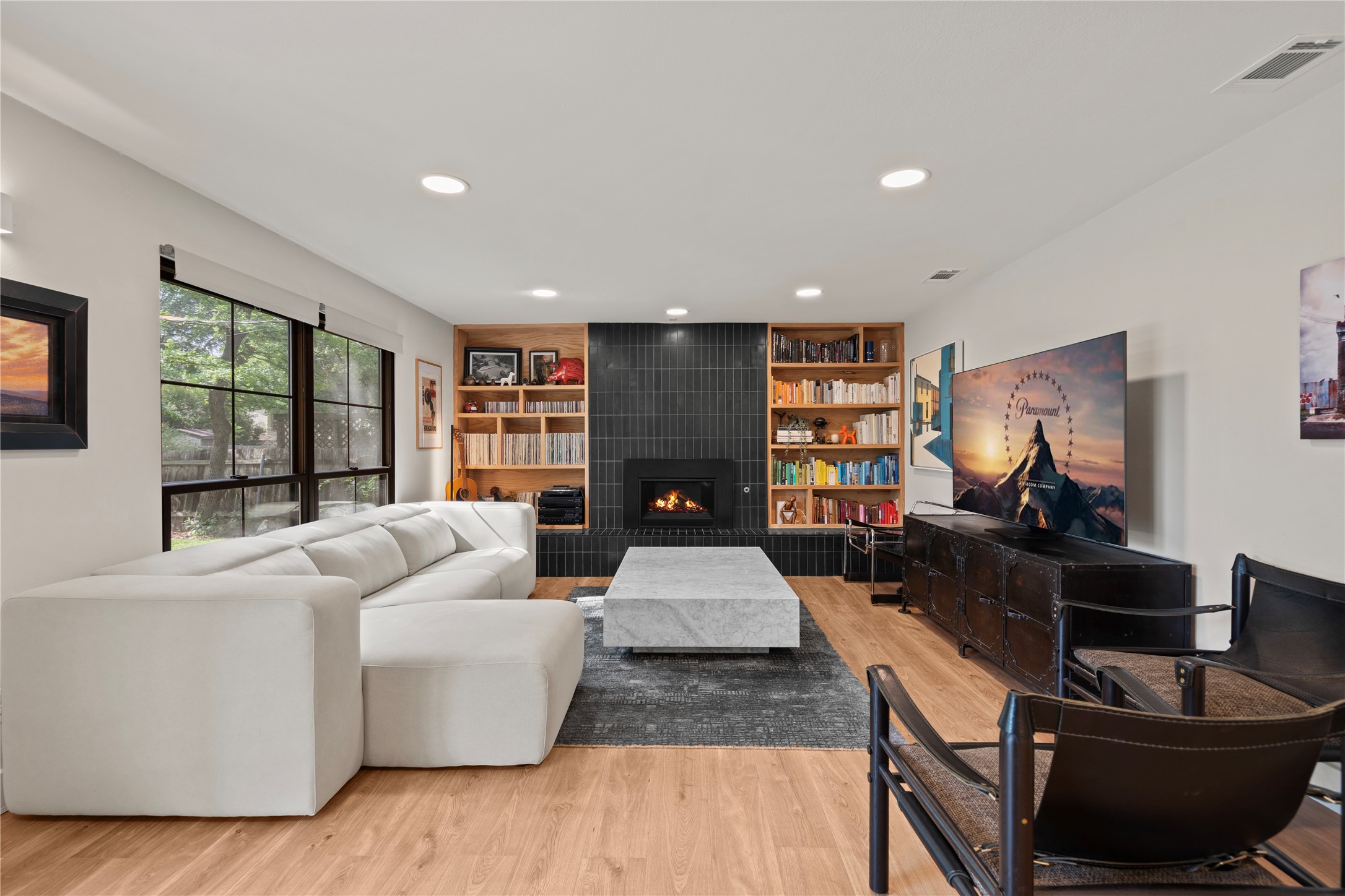 7107 Greenock Street Austin, TX 78749 - Photo 5 of 40 The living area features light wood flooring, a fireplace with a dark tile surround, built-in shelving, and large windows