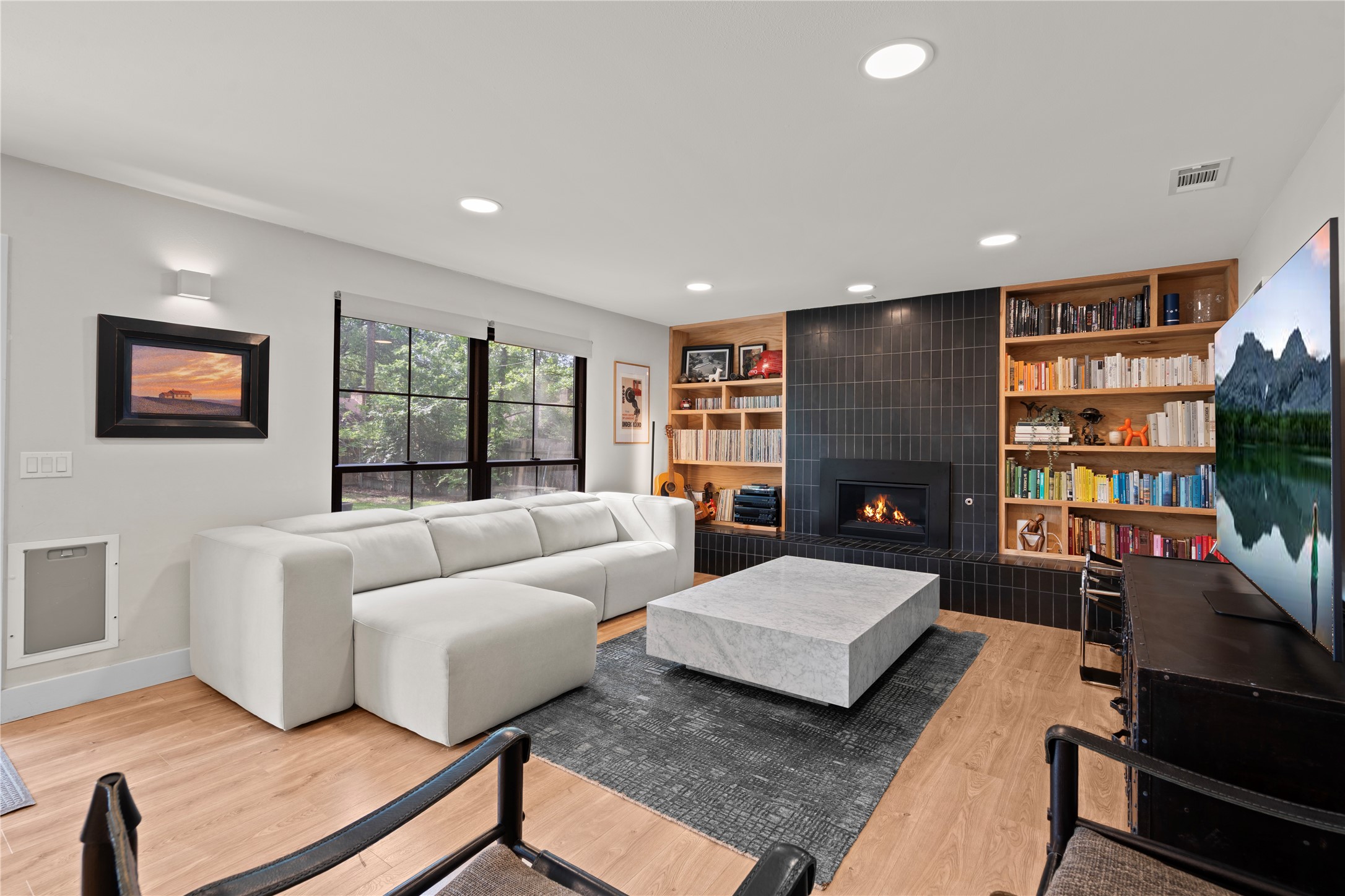 7107 Greenock Street Austin, TX 78749 - Photo 6 of 40 Living area featuring hardwood floors, large windows providing natural light, a fireplace with dark tile surround, and built-in shelving