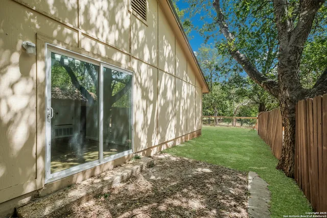 a view of a backyard with large trees and wooden fence