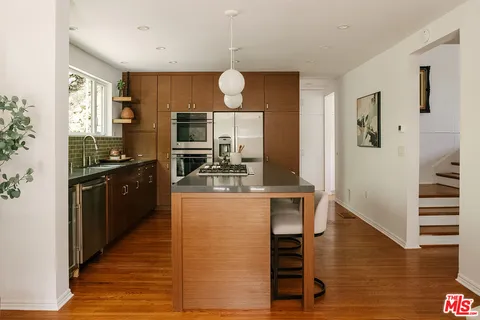 a kitchen with stainless steel appliances granite countertop a refrigerator a sink dishwasher a stove and a dining table with wooden floor