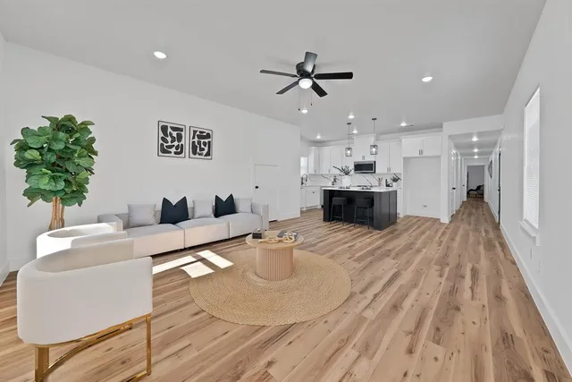 a living room with kitchen island furniture a chandelier wooden floor and a kitchen view