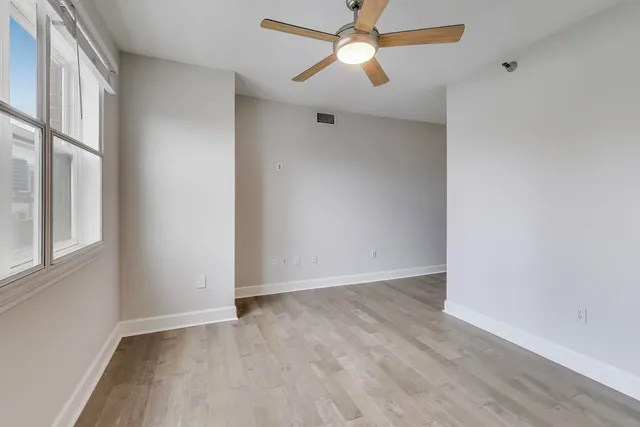 an empty room with wooden floor fan and windows