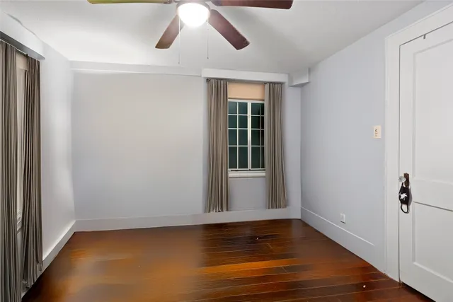 a view of an empty room with wooden floor and fan