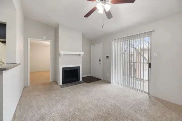 a view of a livingroom with a fireplace a ceiling fan and kitchen view