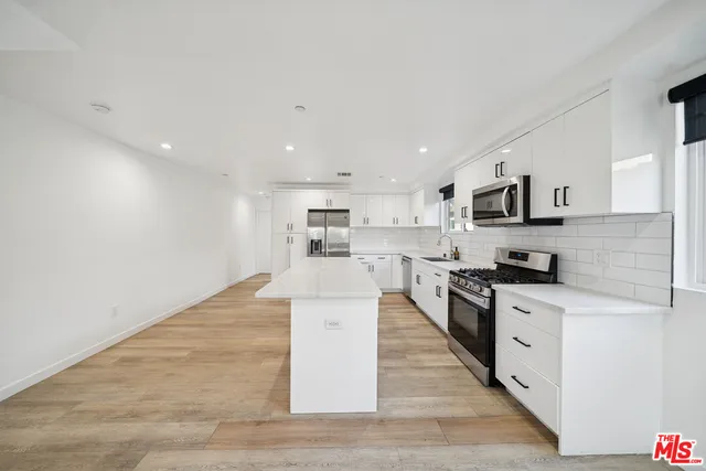 a large kitchen with stainless steel appliances granite countertop a stove top oven a sink dishwasher and a refrigerator with wooden floor