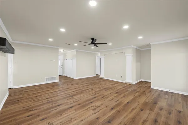a view of an empty room with wooden floor and a ceiling fan