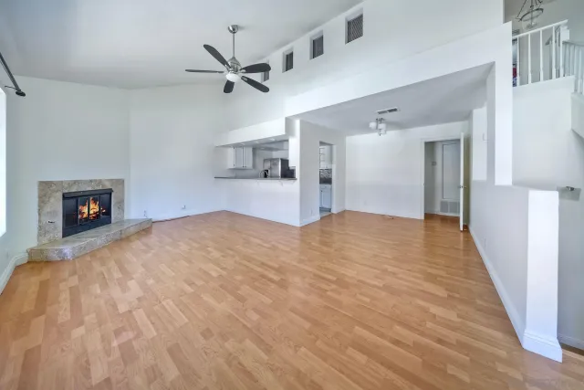 a big room with wooden floor a ceiling fan and kitchen space