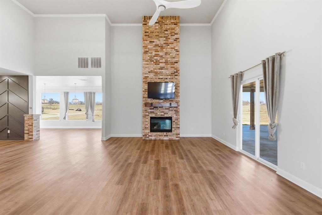 4600 Old Brock Road Weatherford, TX 76087 - Photo 7 of 40 Unfurnished living room with a high ceiling, a fireplace, light wood finished floors, ornamental molding, and ceiling fan
