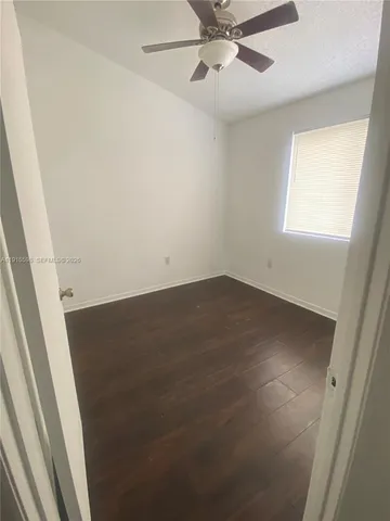 an empty room with wooden floor fan and windows
