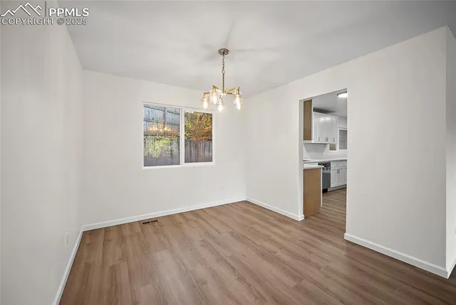 an empty room with wooden floor chandelier and windows