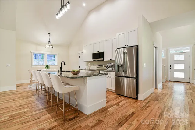 a kitchen with stainless steel appliances a dining table chairs a refrigerator and cabinets