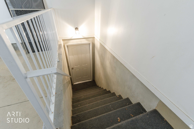 2327 Bluff Ridge Drive Syracuse, UT 84075 - Photo 44 of 66 Carpeted staircase with white balusters and handrail, featuring a wall-mounted light fixture and a paneled door at the bottom
