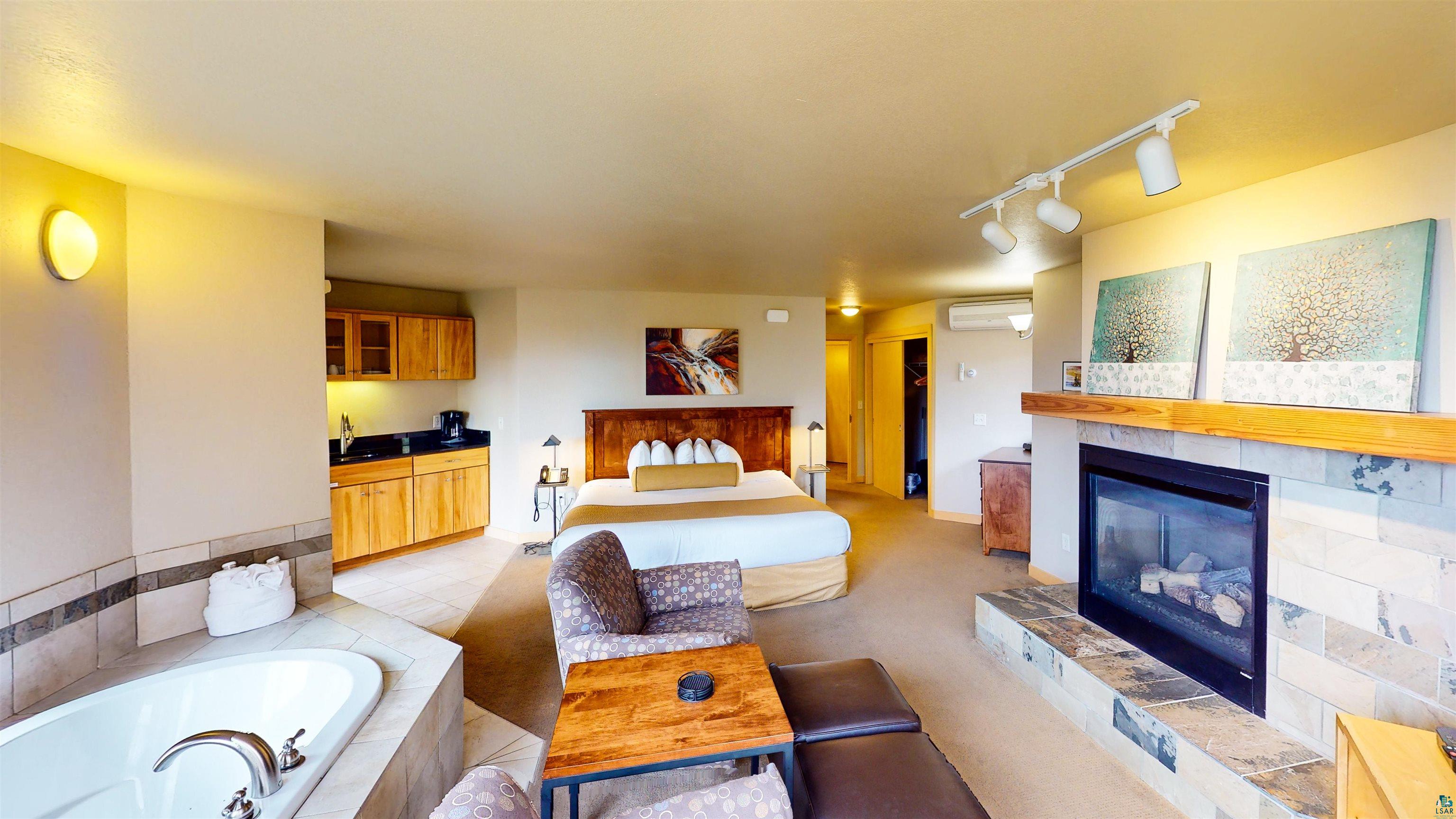 40 Surfside Drive, Unit 5D Tofte, MN 55615 - Photo 25 of 37 Integrated living space featuring a built-in jetted tub, a fireplace with a stone surround and wood mantel, a kitchenette with wood cabinetry and a black countertop, and track lighting