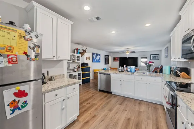 a kitchen with granite countertop a sink dishwasher stove and white cabinets with wooden floor