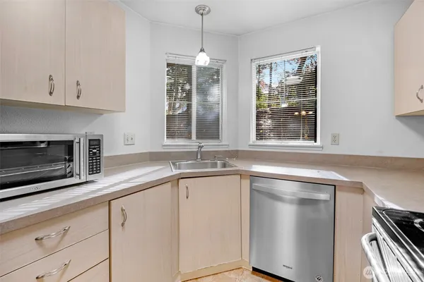 an empty room with a chandelier fan and kitchen view