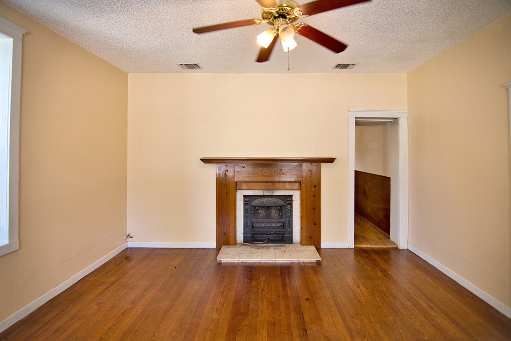 117 Robin Avenue Mason, TX 76856 - Photo 9 of 22 an empty room with wooden floor a ceiling fan and a fireplace
