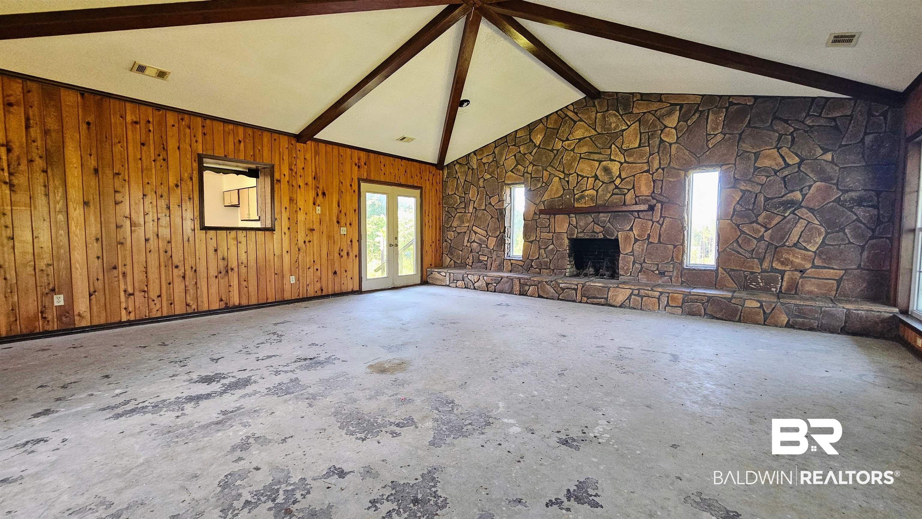 18824 Highway 41 Brewton, AL 36426 - Photo 18 of 40 Spacious room featuring a vaulted ceiling with exposed wood beams, a stone accent wall with a fireplace, wood paneling, and double glass doors