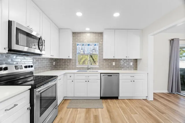 a kitchen with granite countertop white cabinets stainless steel appliances a sink and a window