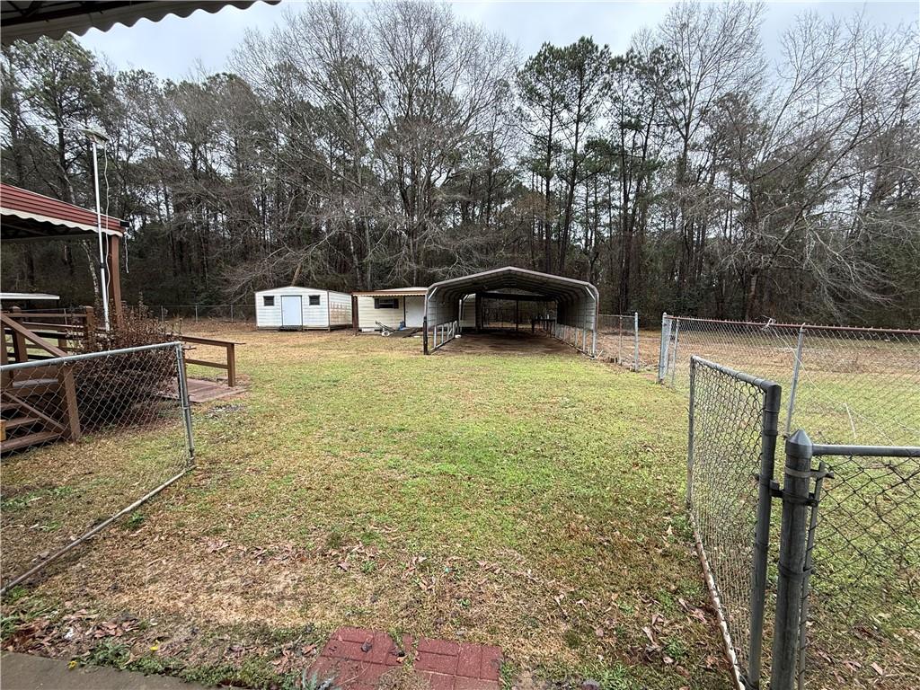 129 Bishop Road Smiths Station, AL 36877 - Photo 6 of 24 View of yard with a gate, a carport, a shed, and view of wooded area