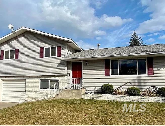 Tri-level home featuring roof with shingles, a front yard, an attached garage, and concrete driveway