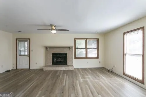 a view of an empty room with wooden floor fireplace and a window