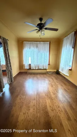 an empty room with wooden floor fan and windows