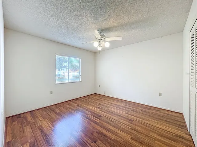 an empty room with wooden floor chandelier fan and windows